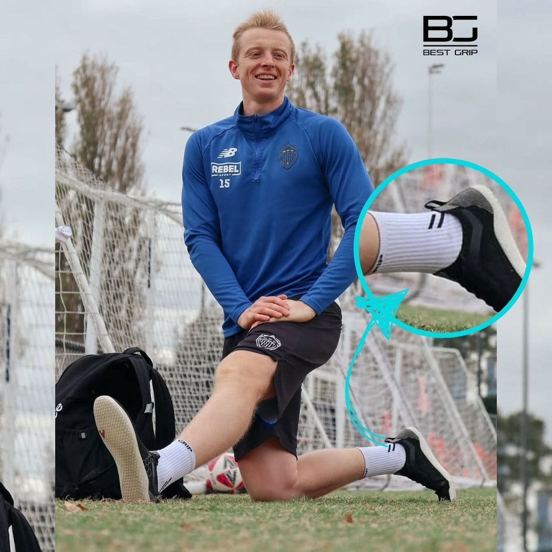 Football player stretching before training while wearing white Best Grip crew grip socks with premium anti-slip silicone grip technology. Close-up showcases the secure locked-in fit inside football boots, designed to reduce foot movement, improve traction, stability, comfort and performance for football and other field sports.